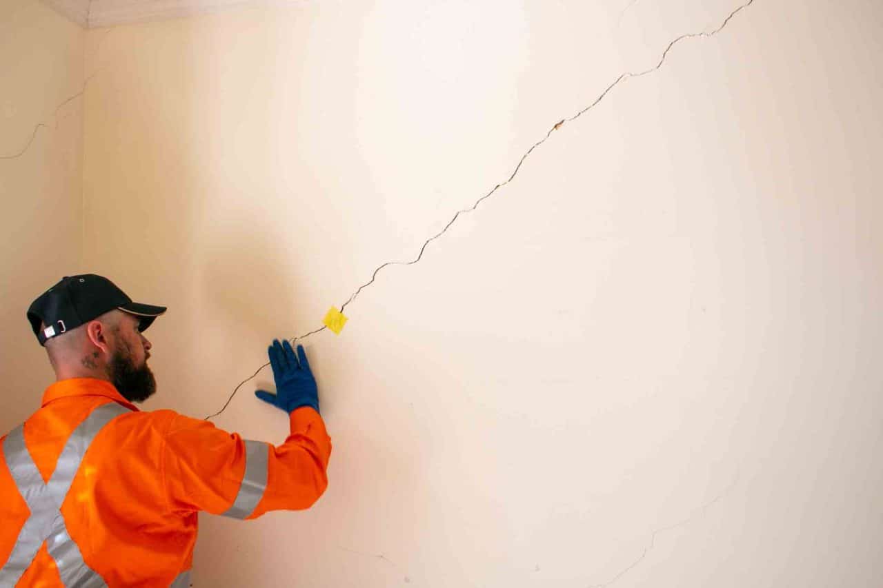 Ingénieur en stabilité inspectant des fissures dans un mur de maison en Belgique