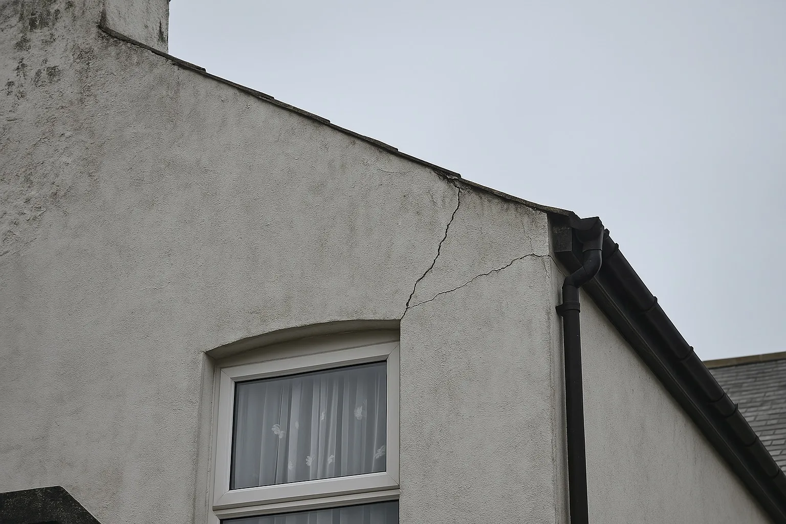 Fissure diagonale au-dessus d’une fenêtre dans un mur de maison.